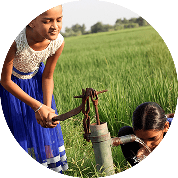 Community members using a hand-operated water pump near agricultural fields